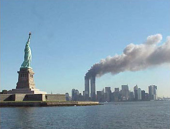 9/11 photo of the World Trade Center in flames, with the Statue of Liberty in the foreground.