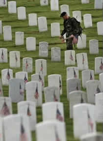Soldier placing American flags on graves in a military cemetery.